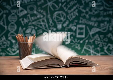 Tables in front of the blackboard drawing open the book and a pen container Stock Photo