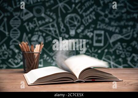 Tables in front of the blackboard drawing open the book and a pen container Stock Photo