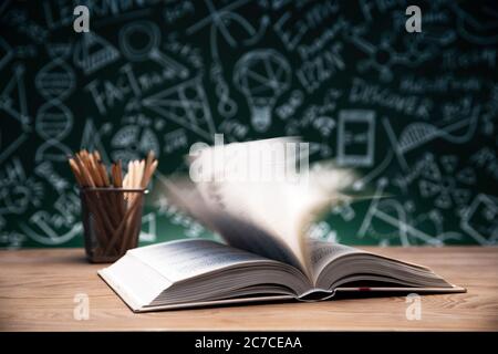 Tables in front of the blackboard drawing open the book and a pen container Stock Photo