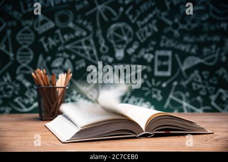 Tables in front of the blackboard drawing open the book and a pen container Stock Photo