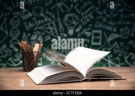 Tables in front of the blackboard drawing open the book and a pen container Stock Photo