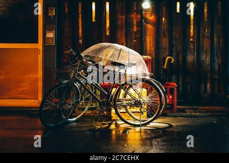 Wide shot of black road bicycles on the street with a clear umbrella on a rainy evening Stock Photo