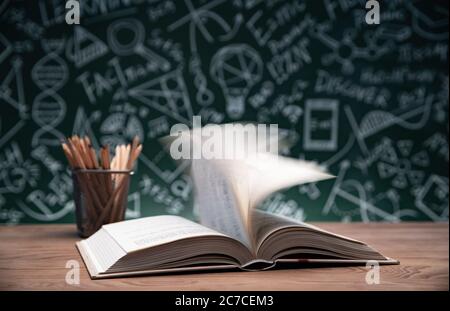 Tables in front of the blackboard drawing open the book and a pen container Stock Photo