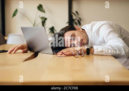 Young tired man with laptop sleeping on desk at work in office Stock Photo
