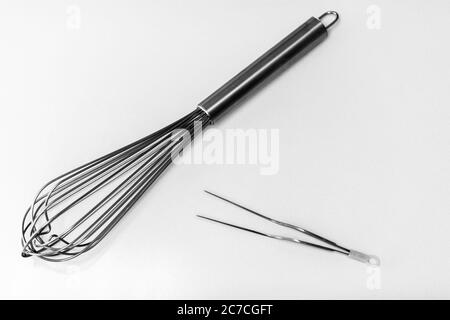 High angle greyscale shot of whisks and tongs on a white surface Stock Photo