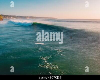 Aerial view of big stormy waves and surfer at sunset time. Biggest ocean wave in Bali Stock Photo