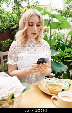 Beautiful young businesswoman eating lunch in cafe and checking e-mails and text messages from friends and clients on her smartphone Stock Photo