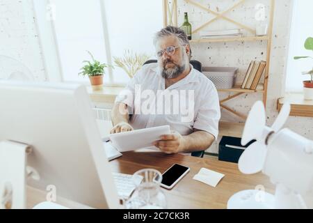 Upset. Businessman, manager in office with computer and fan cooling off, feeling hot, flushed. Using fan but still suffering of uncomfortable climate in cabinet. Summer, office working, business. Stock Photo