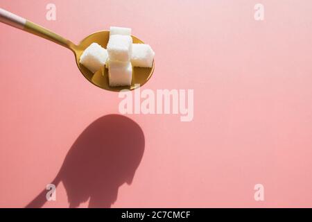 Sugar cubes in golden metal spoon on pink background. Stock Photo