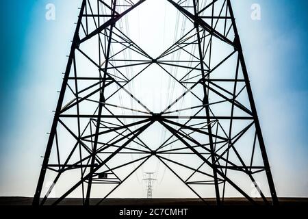 Power lines stretch across a clear sky with a detailed view of the steel tower structure in the foreground, Auvergne Rhone Alpes, France Stock Photo