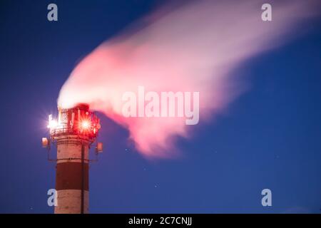 Telecommunications Cell Phone Towers With Antennas Installed On Factory Chimney. Plant Pipe With Escaping Steam Or Smoke In Night Stock Photo