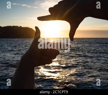 Hands catch sun at sunset time. Female fingers hold sun above lake level. Stock Photo