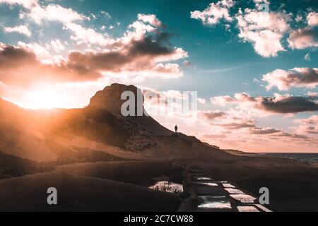 Beautiful wide shot of a person standing on a rocky mountain during sunset under a cloudy blue sky Stock Photo