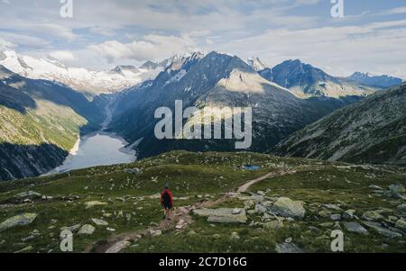 Adventurous man on the edge of a cliff overlooking the beautiful Austria Alps and Lake during a vibrant summer sunset. Taken in Hiking to the Olperer Stock Photo