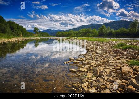 Mountain river stream of water in the rocks with blue sky. Clear river with rocks leads towards mountains Stock Photo