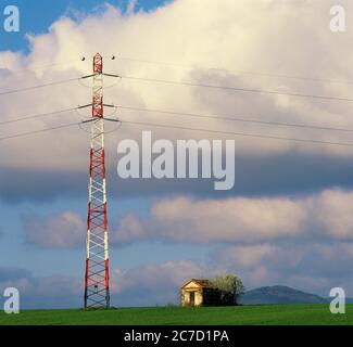 Power lines stand against a backdrop of blue skies and fluffy clouds near a small countryside building. France Stock Photo