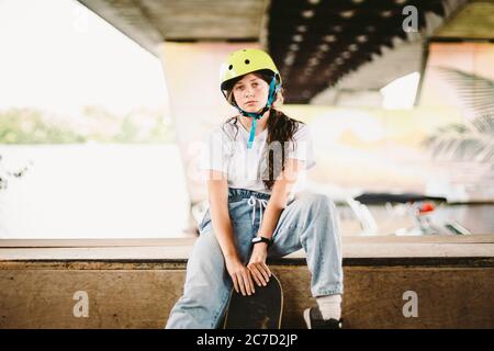 Portrait confident, cool young female skateboarder at outdoor skate park. Urban girl with skate board on half pipe ramp. lifestyle. Teen model Stock Photo