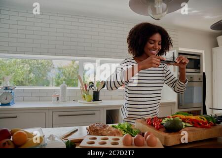 Side video of young successful female food blogger taking picture of freshly slices and chopped vegetables in modern kitchen Stock Photo
