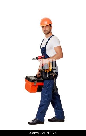 caucasian repairman worker in uniform and helmet holding cordless screwdriver and tool box. handyman wearing tool belt isolated on white studio background Stock Photo