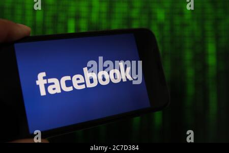 Viersen, Germany - July 9. 2020: View on mobile phone with facebook logo hold by hand. Screen with tunnel of binary code numbers background. Stock Photo