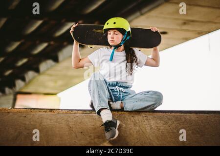 Close up of young attractive girl with skateboard standing outdoors in skate park. Female skateboarder holding her skate behind. Urban skateboarder Stock Photo