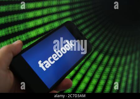 Viersen, Germany - July 9. 2020: View on mobile phone with facebook logo hold by hand. Screen with tunnel of binary code numbers background. Stock Photo