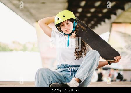 Portrait confident, cool young female skateboarder at outdoor skate park. Urban girl with skate board on half pipe ramp. lifestyle. Teen model Stock Photo