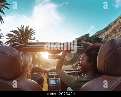 Young happy women doing a road trip in tropical city - Travel people having fun driving in trendy convertible car discovering new places