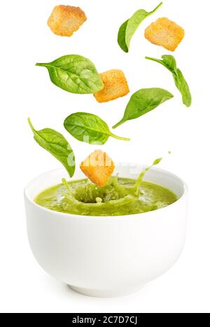 spinach leaves and croutons falling into a soup bowl isolated on white Stock Photo