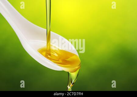 extra virgin olive oil poured in a spoon overflowing on green background Stock Photo
