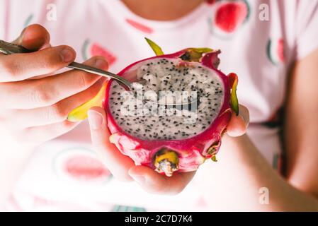 A woman eats with an iron spoon the tropical fruit pitaya. Exotic fruits for a healthy diet. Red dragon fruit. Vegetarian food. Stock Photo