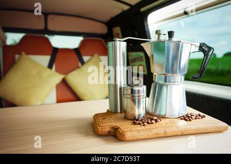 Aqua Bialetti stovetop coffee maker, coffee grinder, chocolate shaker and coffee beans, about to prepare coffee on a wooden tray in a cosy camper van Stock Photo