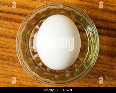 A single white egg in a glass rameking dish from above on a wooden chopping board Stock Photo