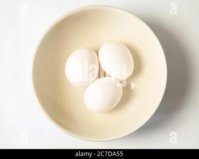 Three white eggs in a bowl centred on a white background Stock Photo