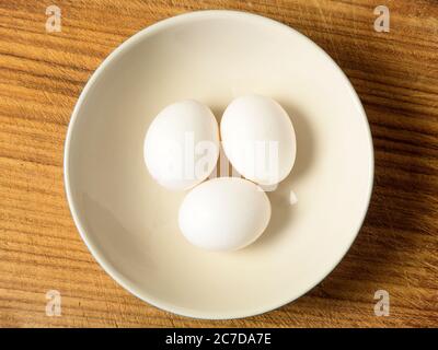 Three white eggs in a bowl centred on a wooden chopping board Stock Photo