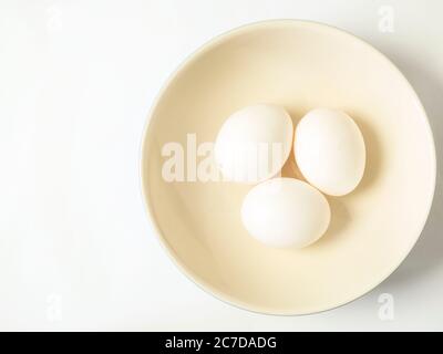 Three white eggs in a bowl offset on a white background with copy space Stock Photo