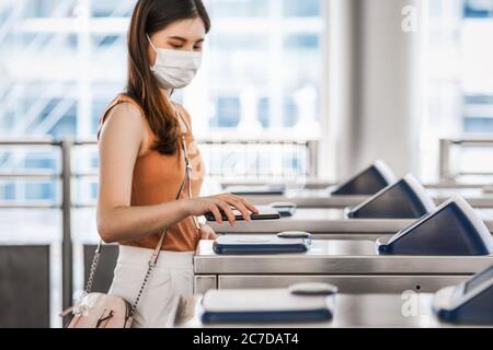Closeup hand using smart mobile phone of Young Asian woman passenger wearing surgical mask for scanning the automatic machine by QR code to subway or Stock Photo