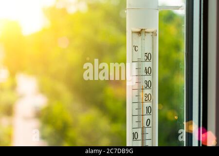 The thermometer outside the window shows a very hot air temperature, heated by the rays of the bright sun Stock Photo