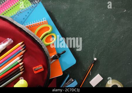 Detail of backpack full of school supplies on green blackboard. Top view Stock Photo