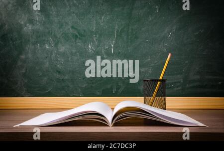Book and pen with pencil and scissors on school desk with blackboard in the background. Concept of studying Stock Photo