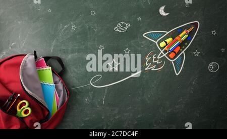 School creativity with drawing on blackboard with colored pencils and school supplies in backpack. Top view Stock Photo