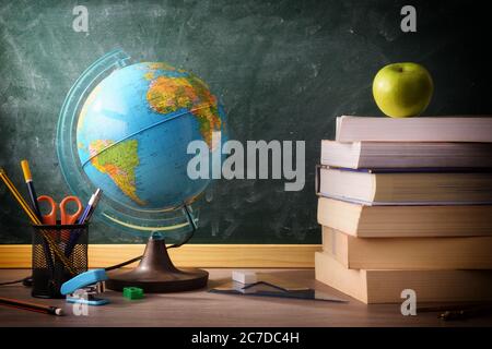Stack of books and school supplies on classroom desk with green blackboard background Stock Photo