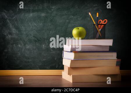 Stack of books with pencil and apple on class table with green chalkboard in background. Concept of studying. Stock Photo