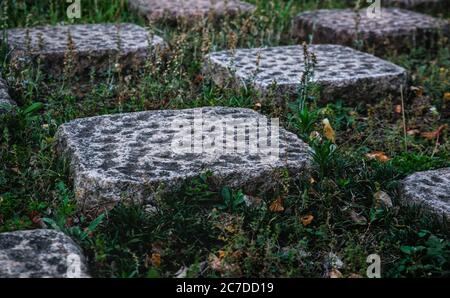 Sidelong perspective of a checkered pattern of dimpled stone tiles and square patches of grass with bits of leaf litter visible Stock Photo