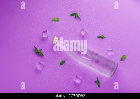 A bottle with an ice drink in drops of condensation, ice cubes and mint leaves on a pink background Stock Photo
