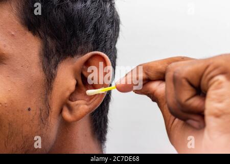 Remove Ear wax Safely - Man cleaning ear with cotton swabs closeup shot. Cleaning ear with cotton bud Dirty ear. Removing ear wax using cotton bud on Stock Photo