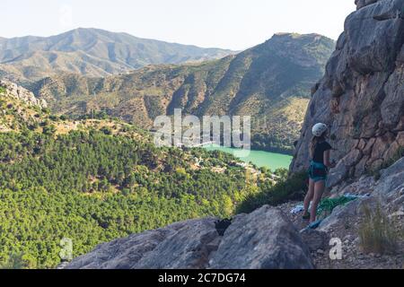 Wide shot of a female climbing a rocky hill surrounded by green mountains and a beautiful lake Stock Photo