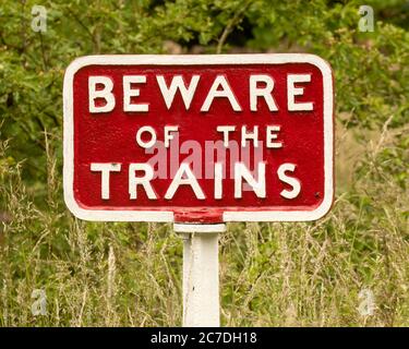 Beware of the Trains sign, cast iron - red with white lettering, against a grassy background Stock Photo