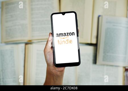Tashkent, Uzbekistan - 27 June 2020: Woman holding mobile phone with Amazon Kindle logo on screen over group of opened books Stock Photo