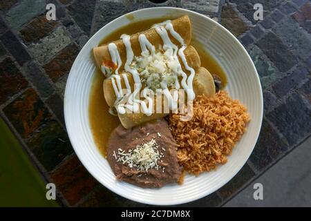 Closeup of a plate of Mexican vegetarian enchiladas with green tomatillo sauce, refried beans and rice from above Stock Photo